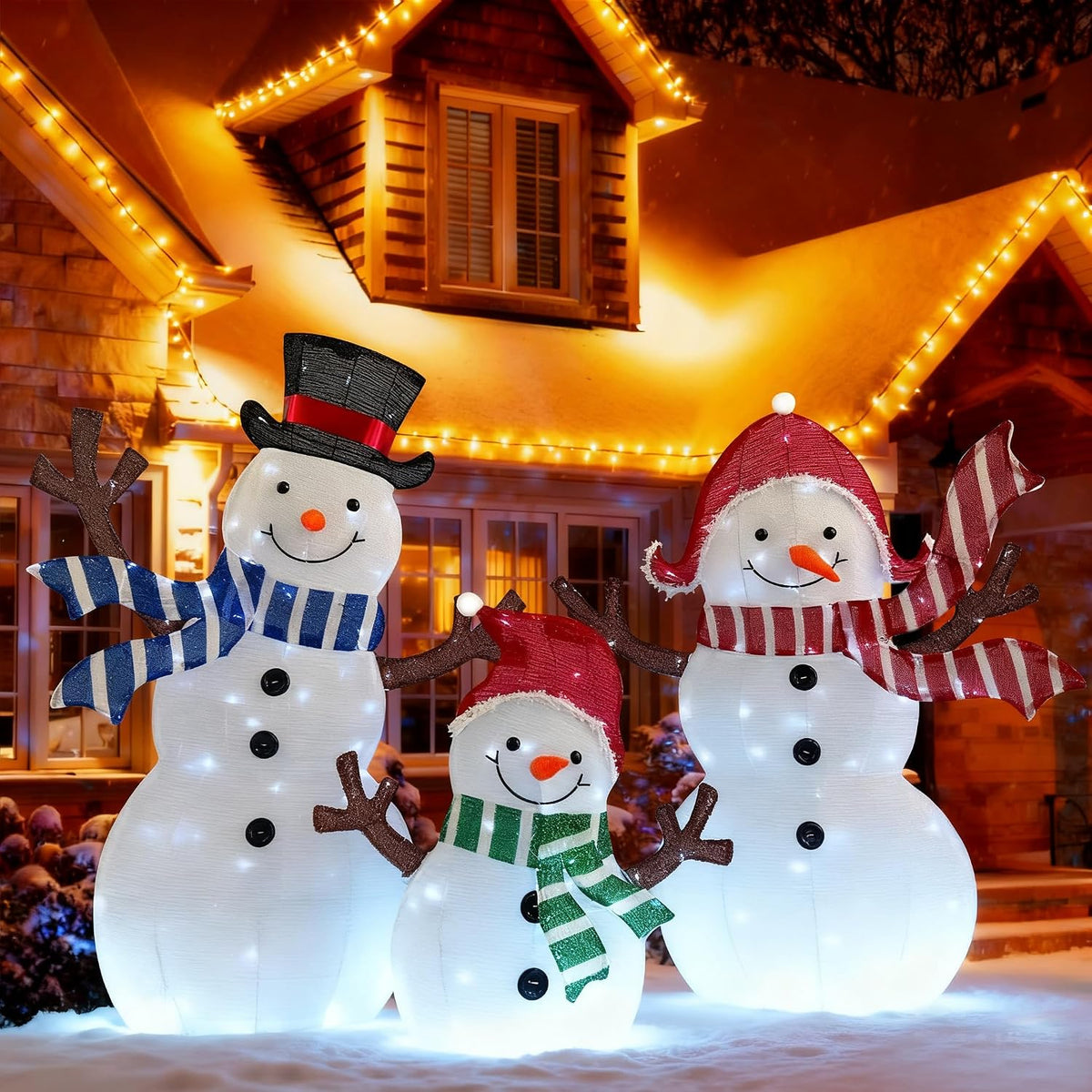 Three lighted snowman figures in hats and scarves glowing in front of a house